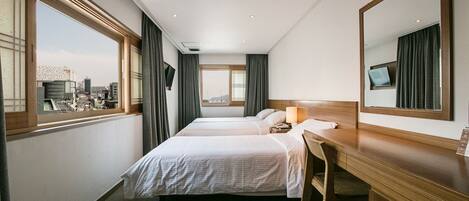 Une chambre d’hôtel avec deux lits, un bureau et une grande fenêtre donnant sur la ville.