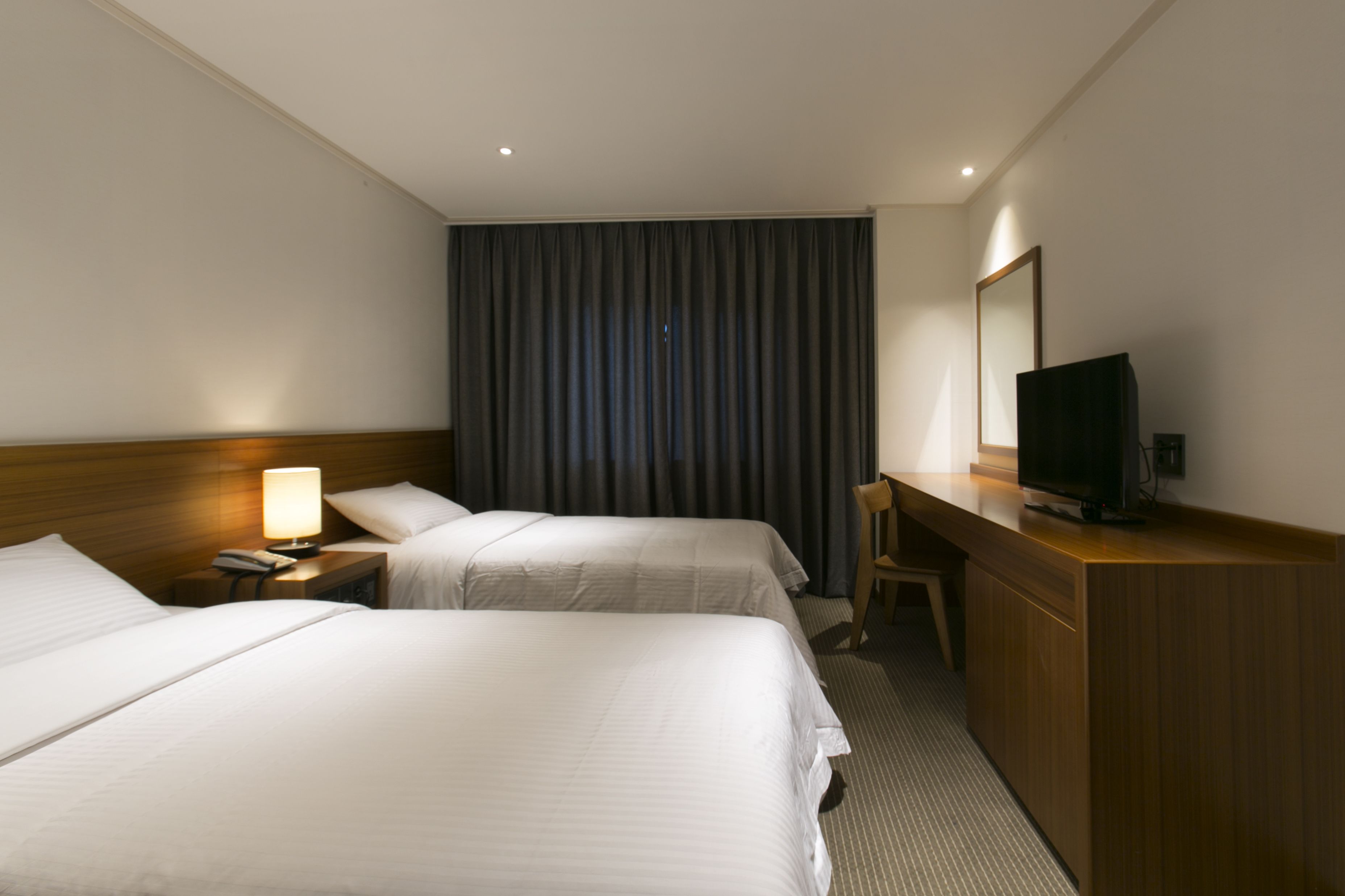 Une chambre d’hôtel avec deux lits, un bureau, une chaise, une télévision et une grande fenêtre avec des rideaux.