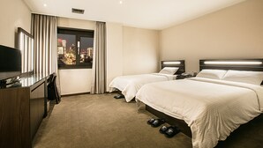Een hotelkamer met twee bedden, een televisie, een bureau en een raam met uitzicht op de stad.