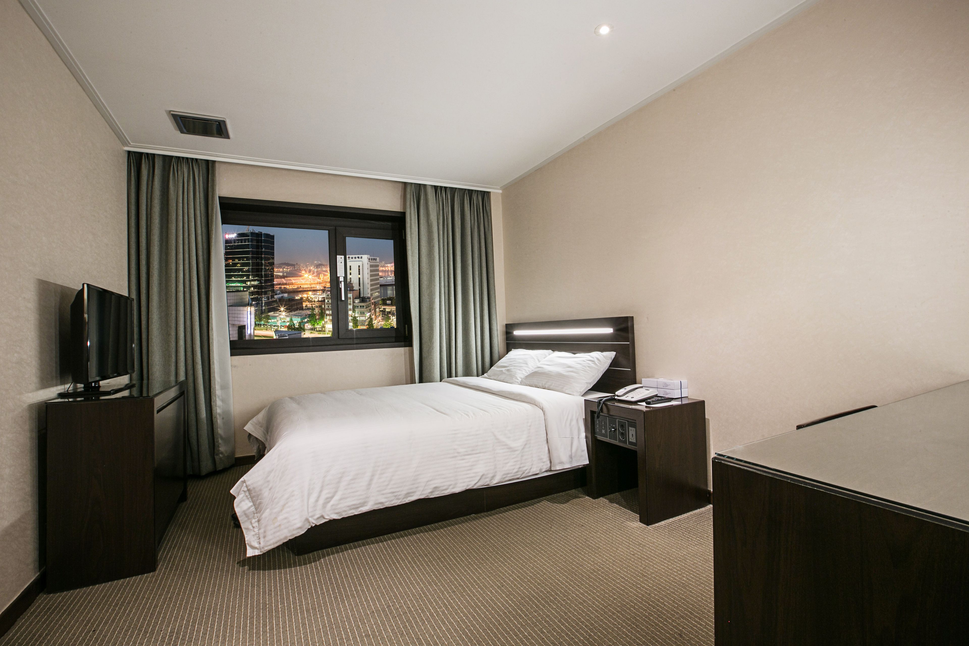 Habitación de hotel con cama, televisor, escritorio y ventana con vistas a la ciudad.