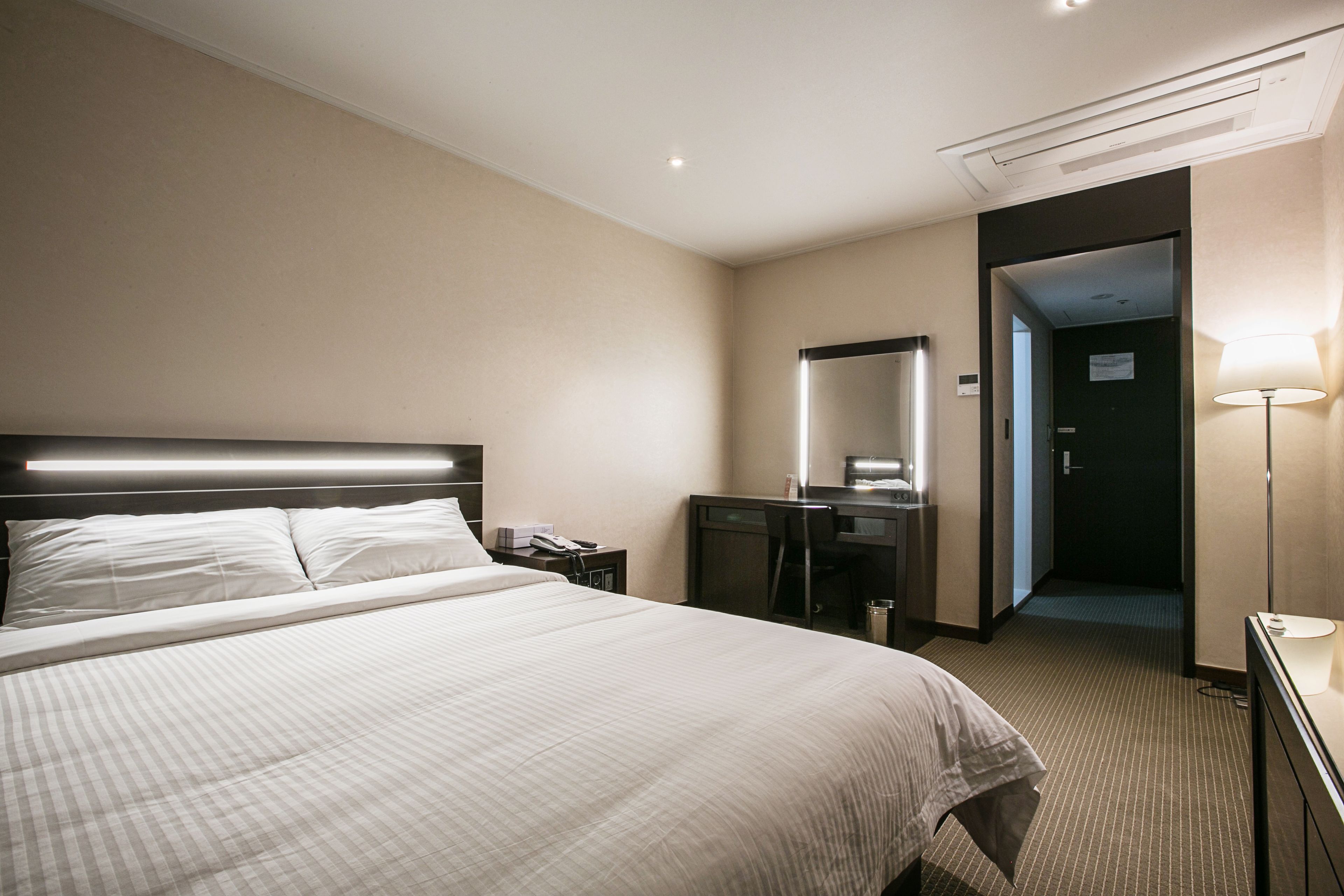 A hotel room with a large bed, a desk, a chair, a desk lamp, and a mirror.