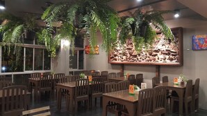 A restaurant interior with wooden tables and chairs, hanging ferns, and a large decorative wall. - T5 Suites at Pattaya (Pattaya)