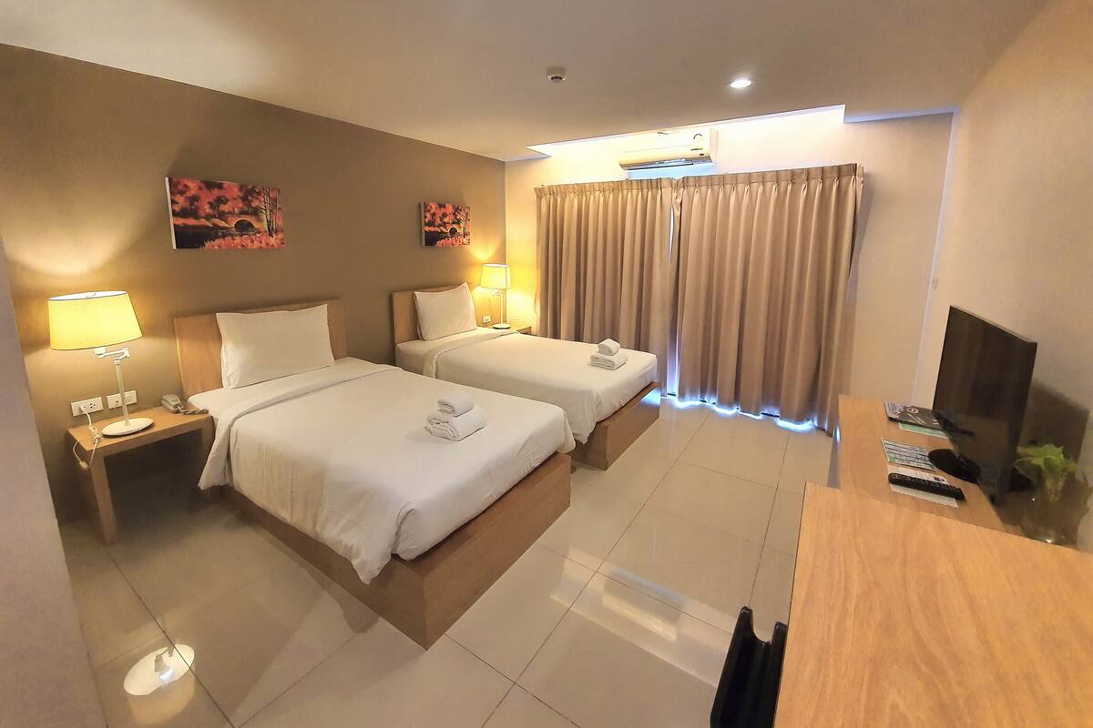 A hotel room with two beds, a desk, a TV, and a window with curtains.