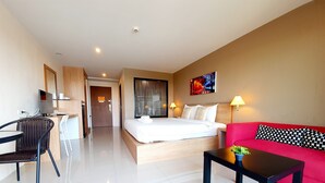 A hotel room with a bed, a red sofa, a desk with a chair, and a small table with a plant. - T5 Suites at Pattaya (Pattaya)