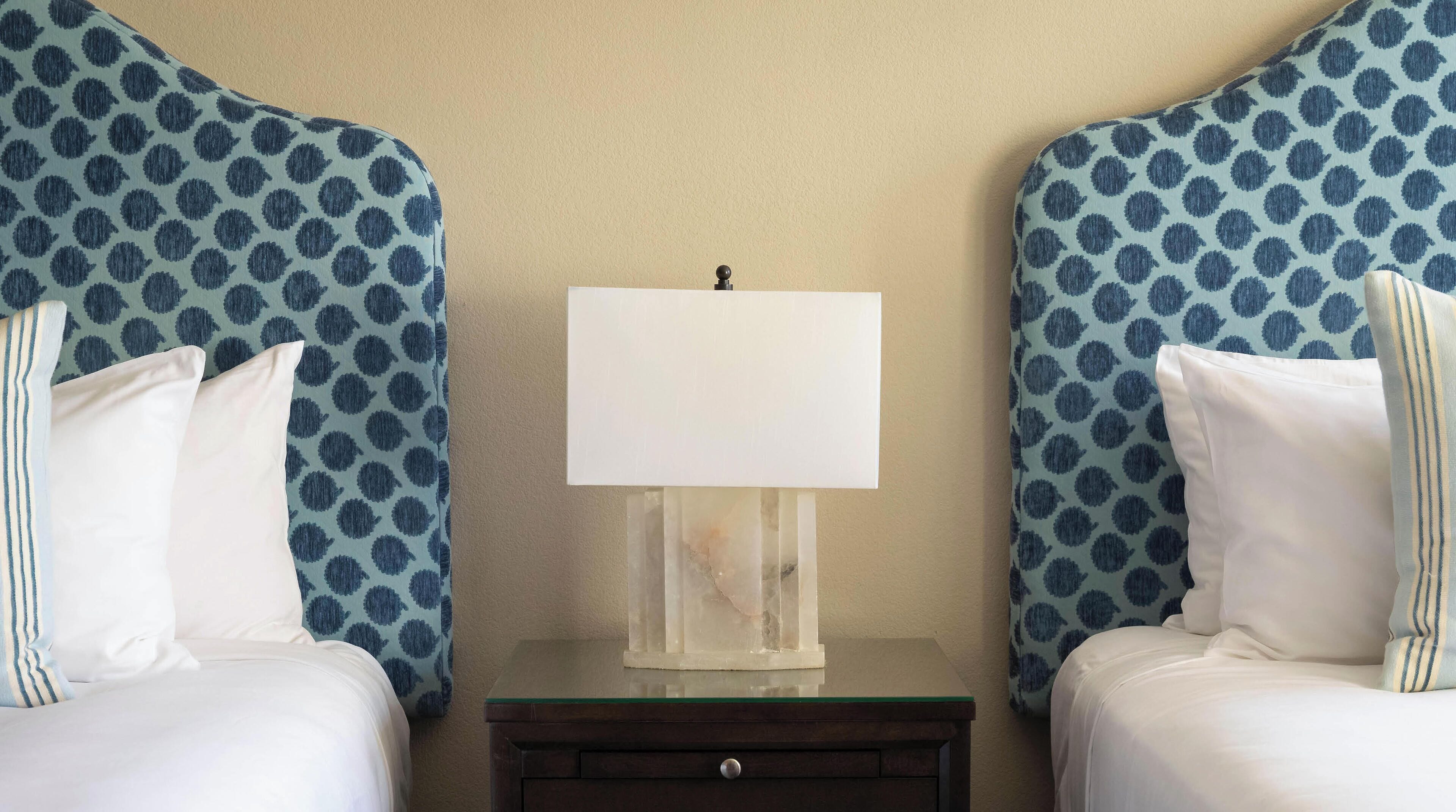 A hotel room with two beds, a nightstand, and a lamp.