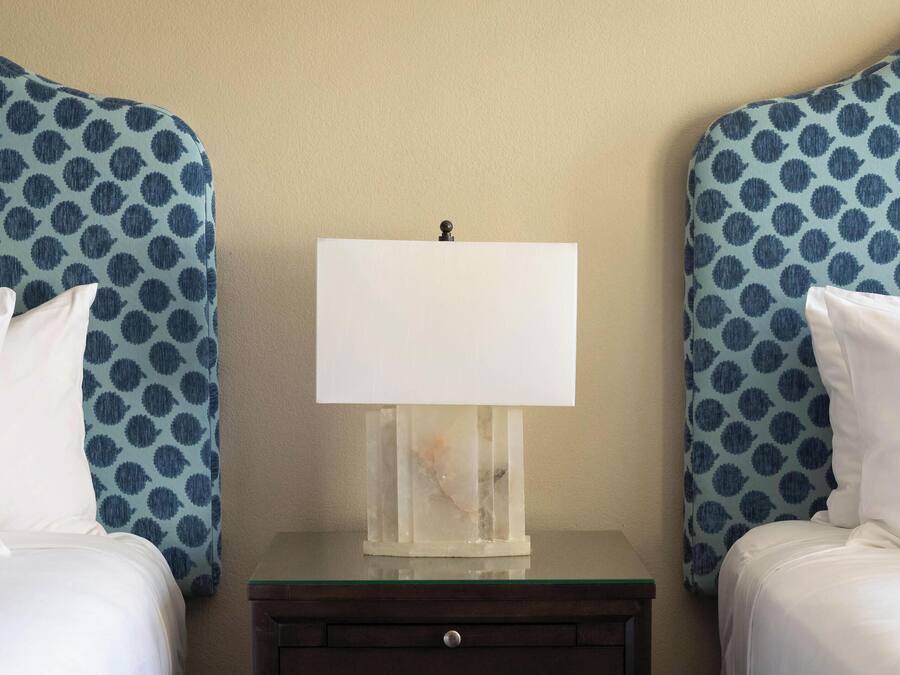 A hotel room with two beds, a nightstand, and a lamp.