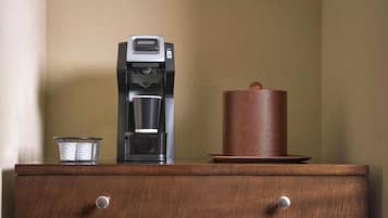 A coffee maker, a candle, and a mesh container on a wooden surface.