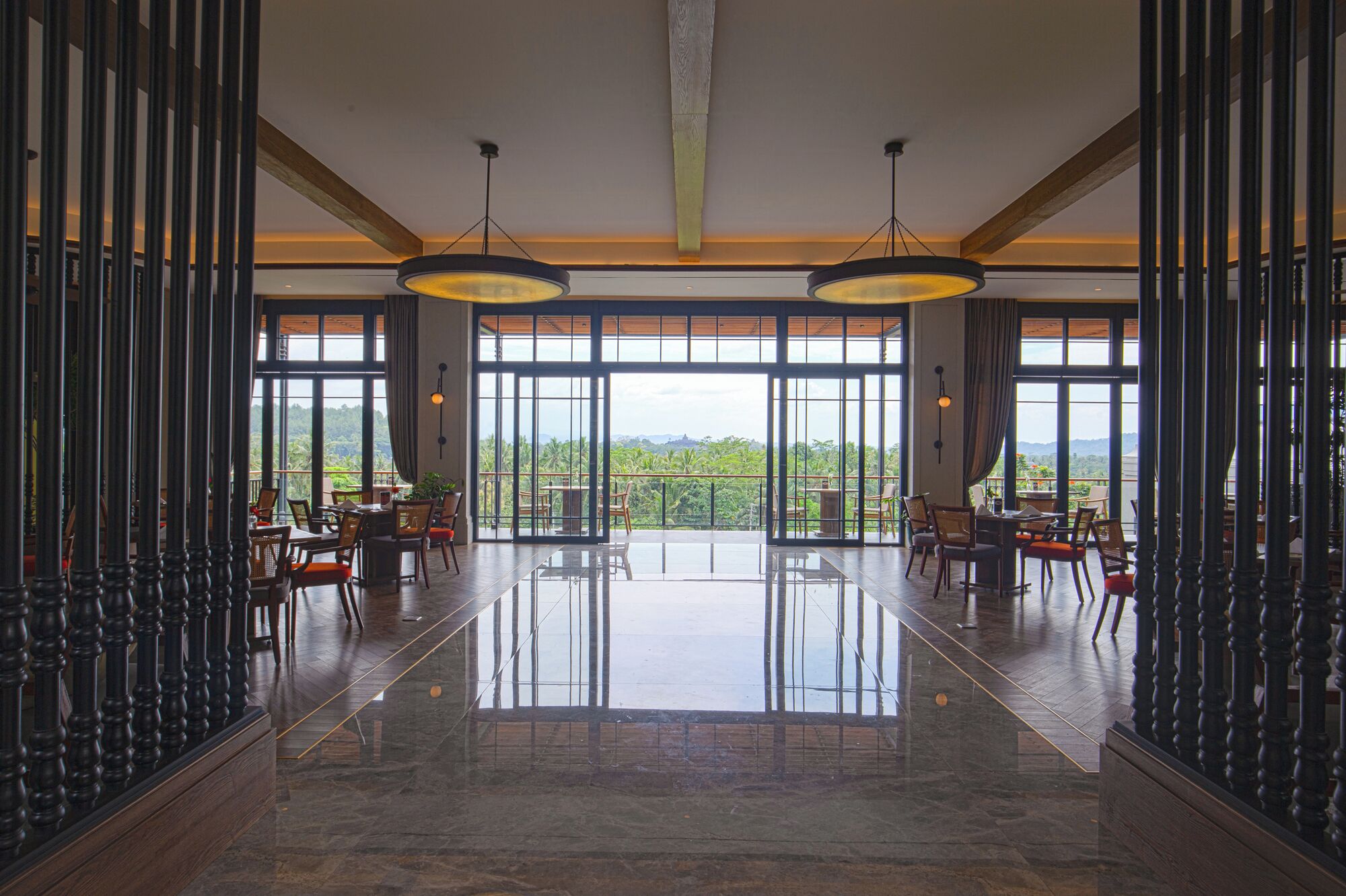 A spacious lobby with a polished marble floor, large windows offering a view of lush greenery, and elegant wooden furniture.