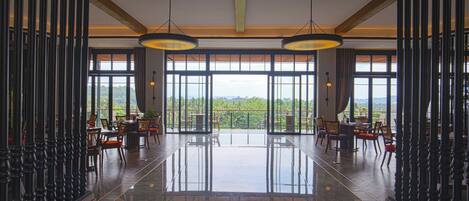 A spacious lobby with a polished marble floor, large windows offering a view of lush greenery, and elegant wooden furniture.