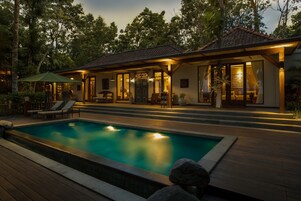 Una casa moderna con piscina, zona de estar exterior y un porche cubierto.