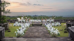 Montaje de ceremonia de boda con un sendero de piedra que lleva a un altar, rodeado de arreglos florales blancos y sillas, con vistas a un paisaje pintoresco.