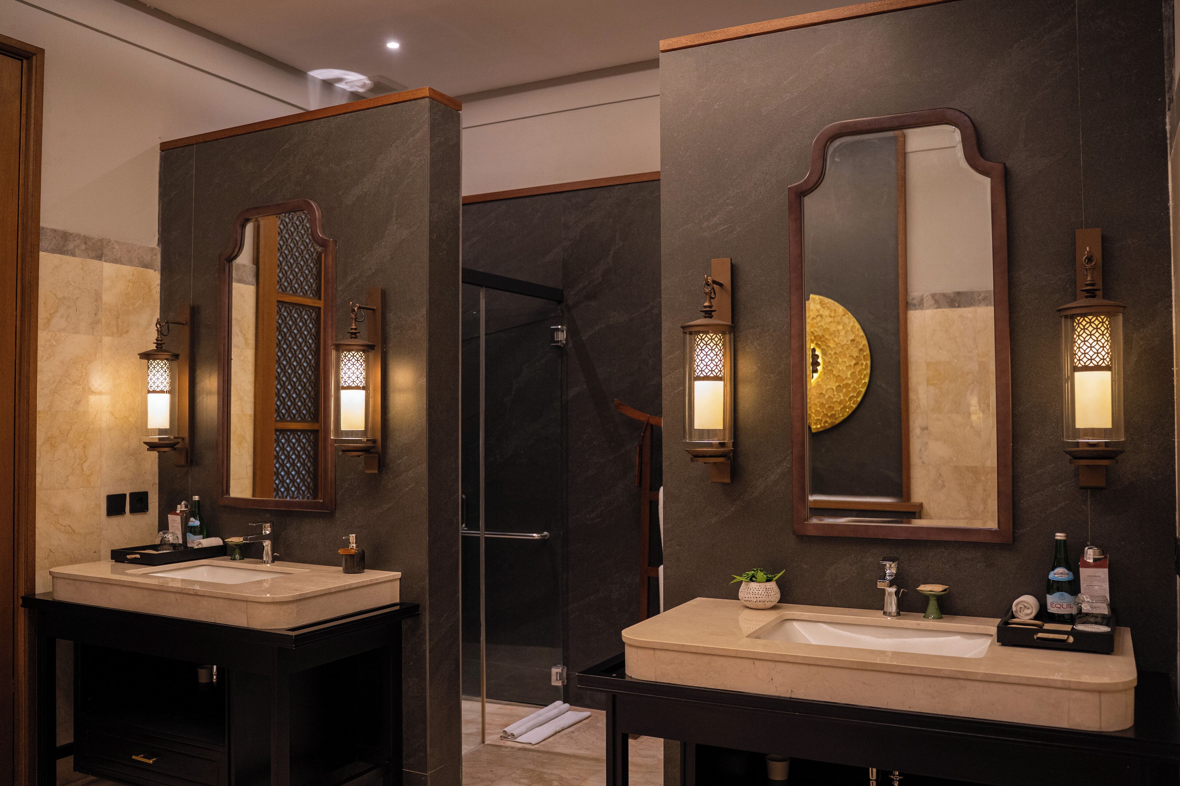 Ein modernes Badezimmer mit zwei Waschbecken, dunklen Marmorwänden und Wandleuchten.
