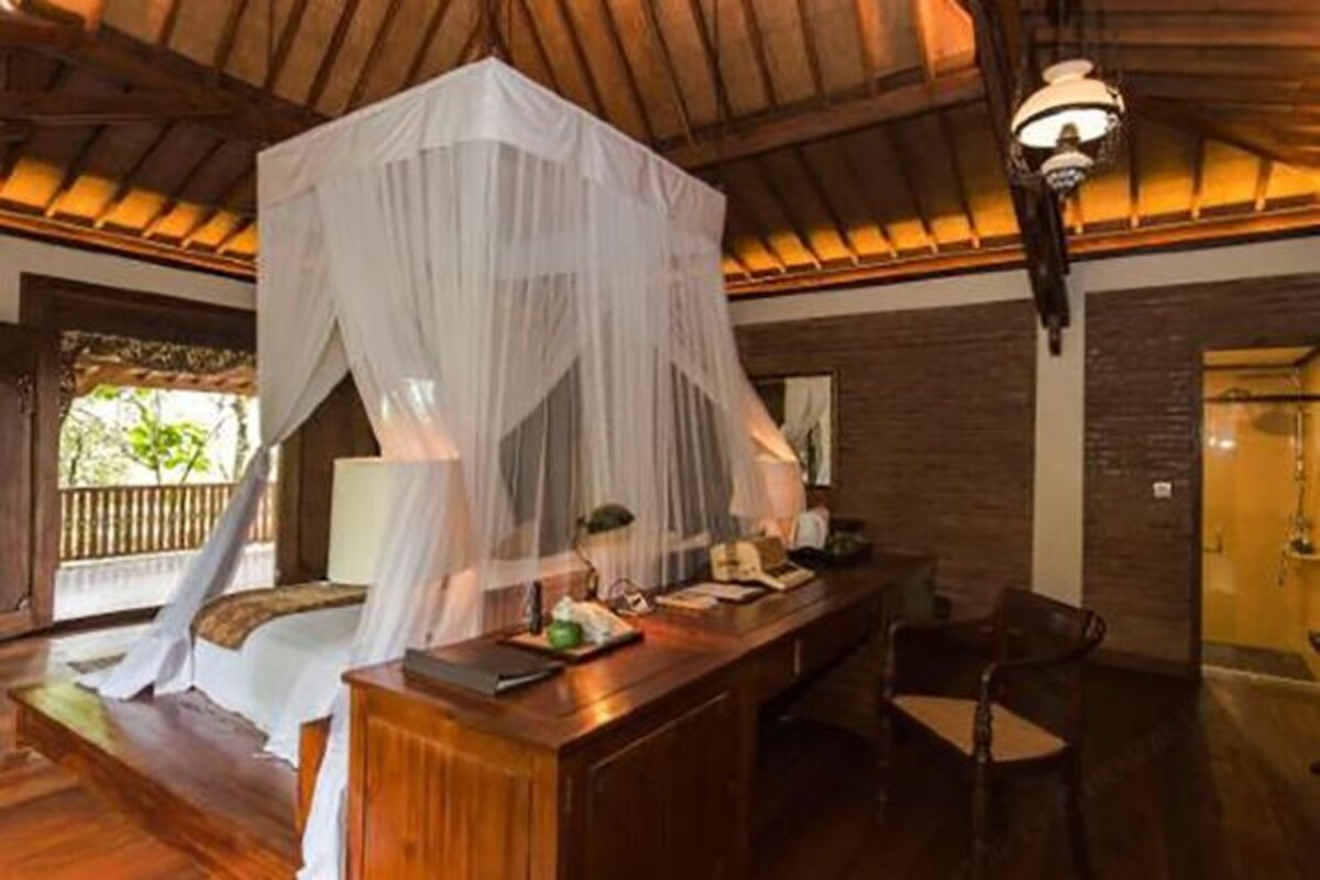 A room with a bed under a canopy, a desk with a chair, and a hanging light fixture.
