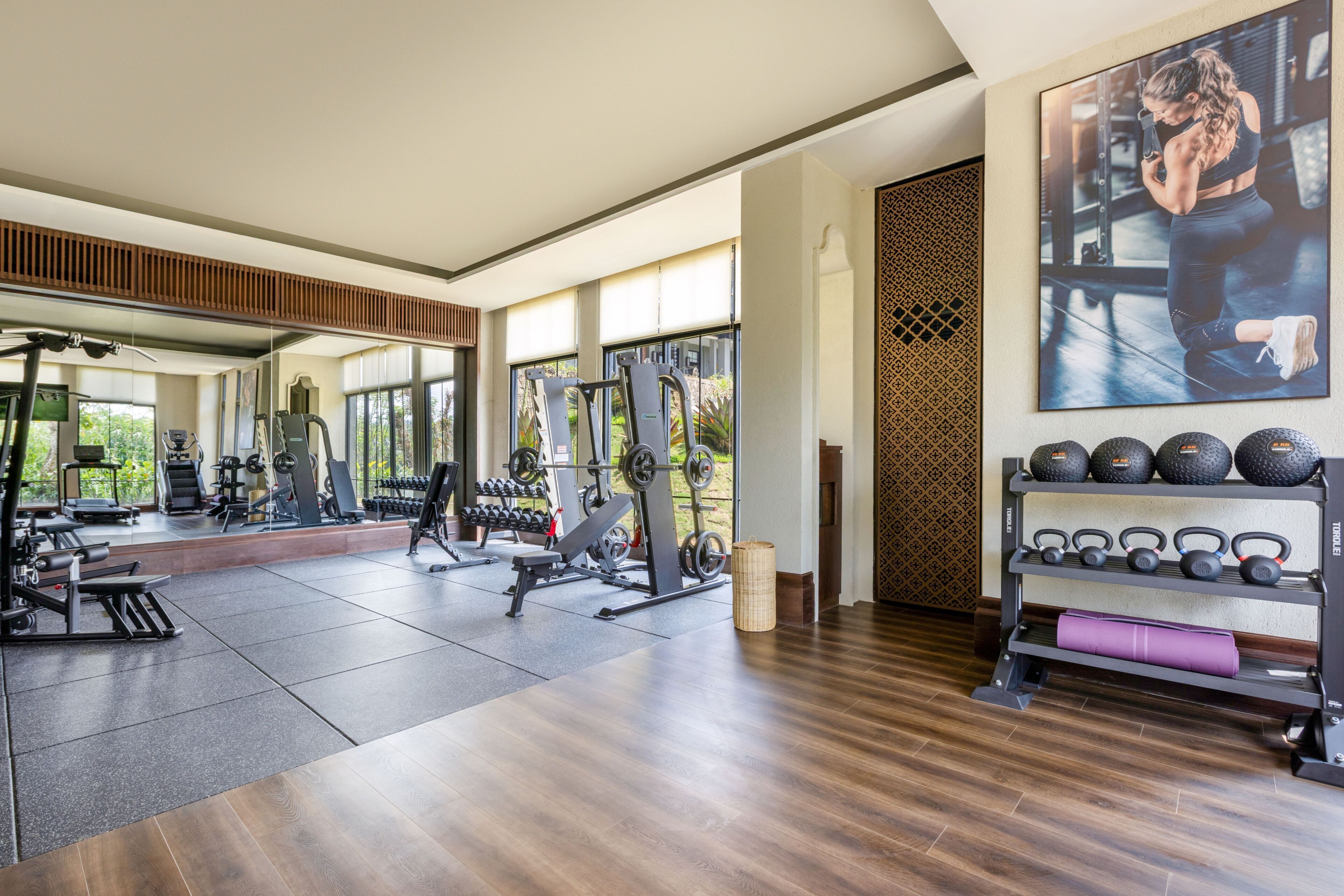 A modern gym with various exercise equipment, large windows, and a mirror.