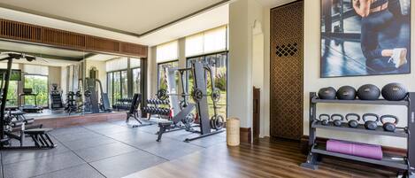 A modern gym with various exercise equipment, large windows, and a mirror.