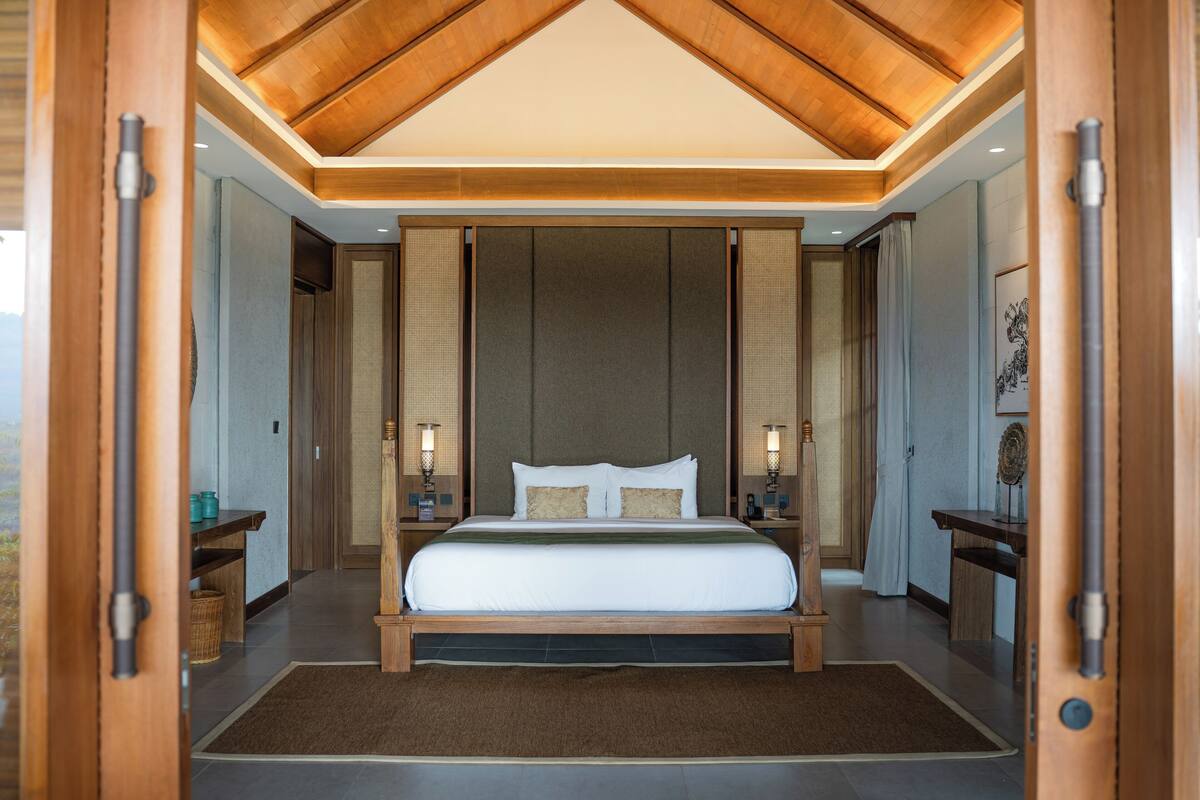 Ein geräumiges Schlafzimmer mit einem großen Bett, einem Holz-Kopfteil und Blick durch eine offene Tür.