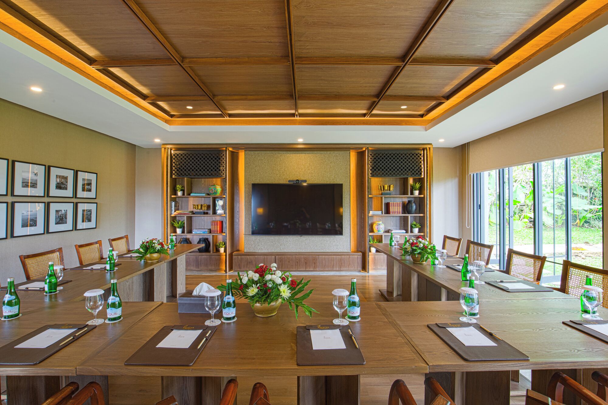A conference room with a long table, chairs, a large screen, and shelves with books and decorative items.