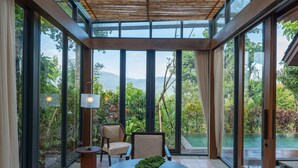 Una habitación moderna con ventanas de vidrio amplias, una mesa redonda con un bol, dos sillas y una mesita auxiliar.