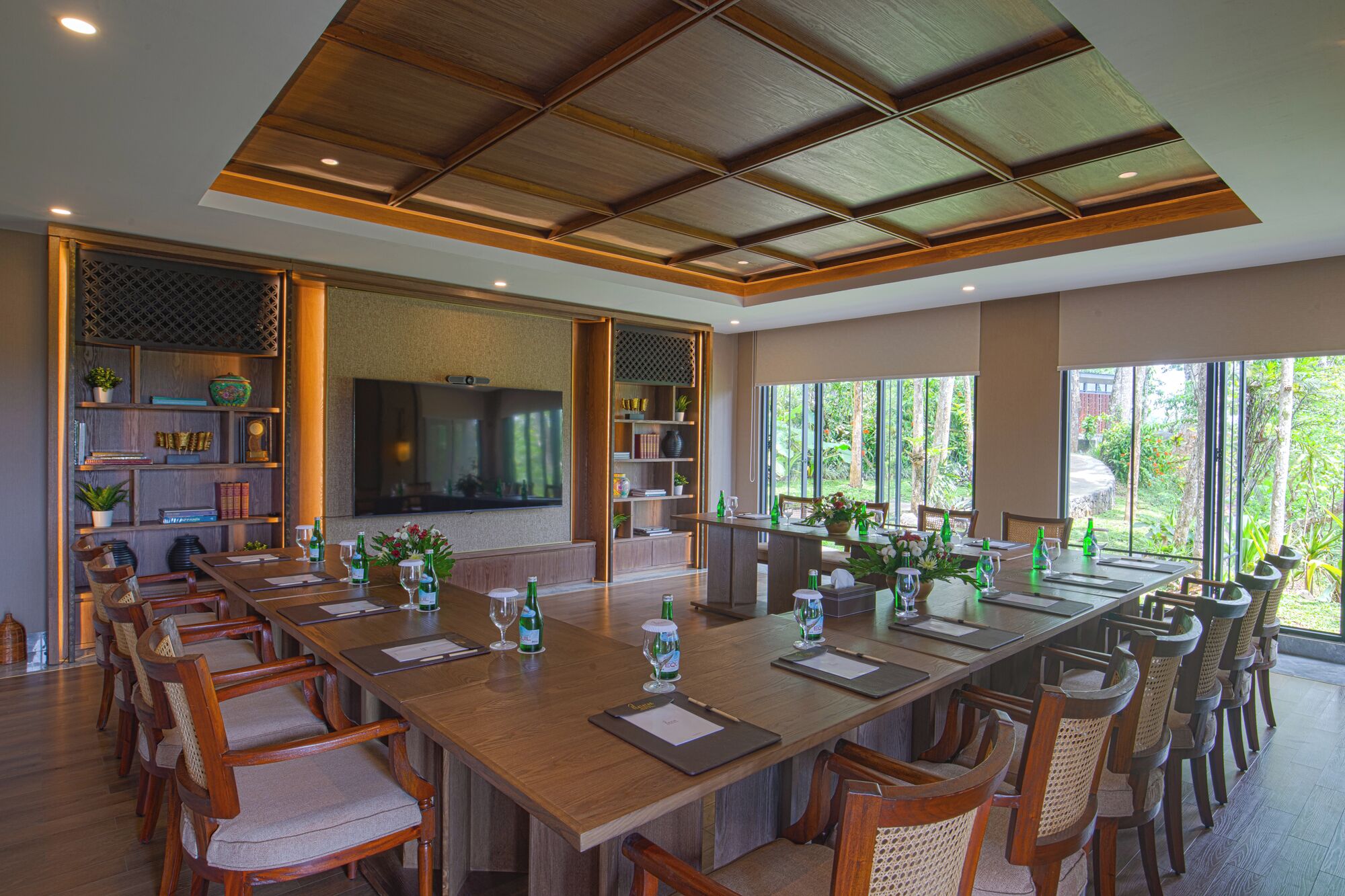 Un vaste espace dédié à la salle à manger, avec une longue table en bois, de nombreuses chaises et un grand téléviseur à écran plat fixé au mur.