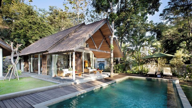 Una casa moderna con piscina, terraza de madera y zona de estar exterior rodeada de exuberante vegetación.