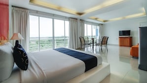 A hotel room with a large bed, a dining table with chairs, a TV, and a view of the outdoors.