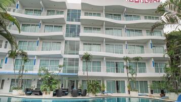 A multi-story hotel with a pool area, featuring balconies and potted plants.