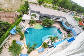A swimming pool with a slide, surrounded by lounge chairs and palm trees, adjacent to a building with a sloped roof. - Capital O 998 The Magnolias Pattaya Boutique Resort (Bang Lamung)