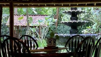 A covered outdoor dining area with a table and chairs, surrounded by lush greenery and a decorative fountain.