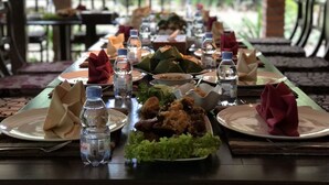 A dining table set with plates, water bottles, and food items, surrounded by chairs and a view of greenery. - Rumah Boedi Private Residence Villa (Borobudur)