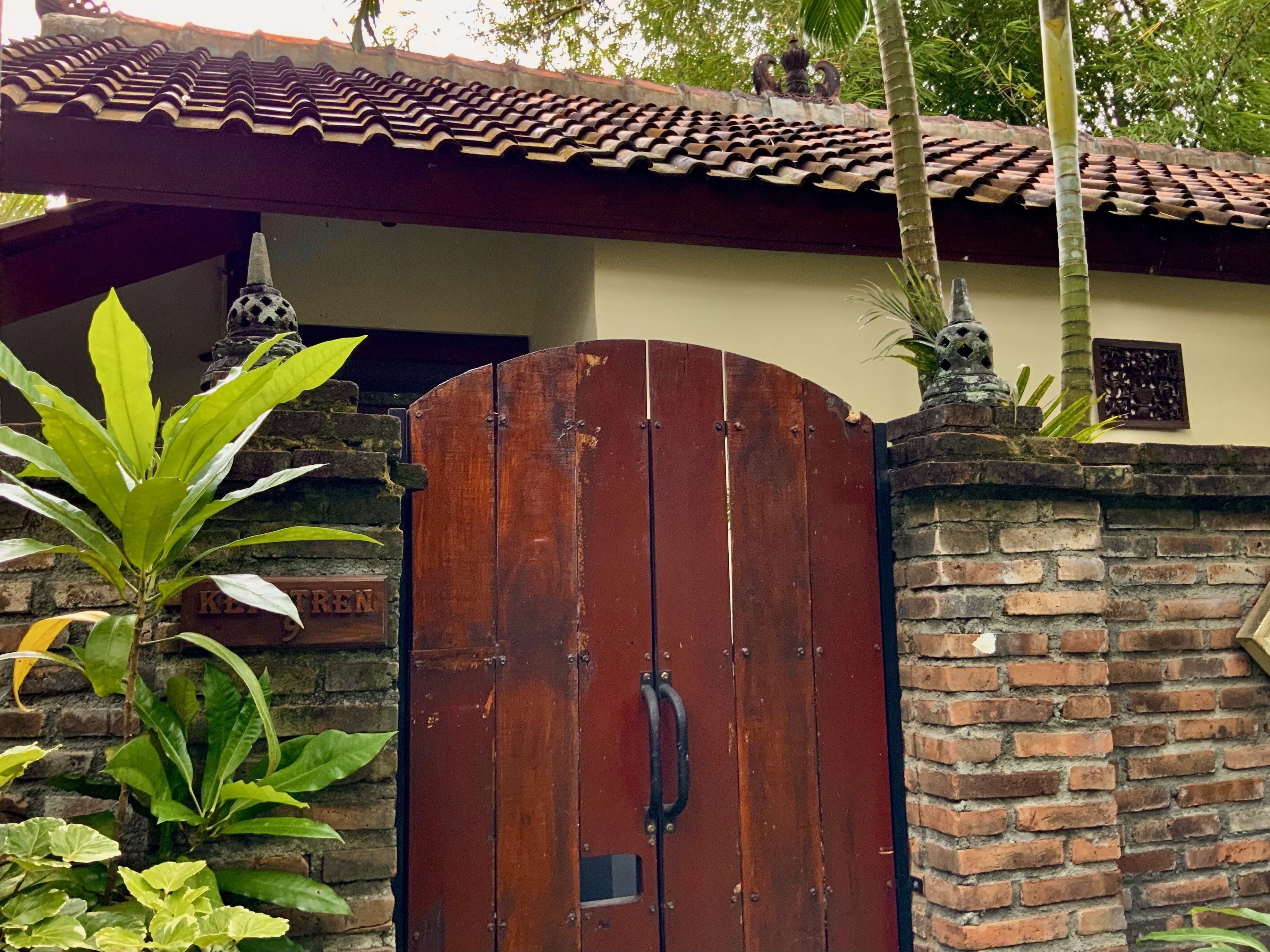 A gated entrance with a wooden door, brick walls, and a tiled roof.