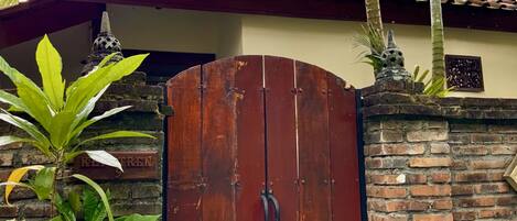 A gated entrance with a wooden door, brick walls, and a tiled roof.
