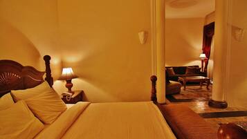 Ein Hotelzimmer mit einem großen Bett, einem hölzernen Kopfteil, einem Nachttisch mit Lampe, einem Sofa und Blick auf den Flur.
