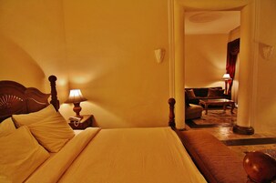 Ein Hotelzimmer mit einem großen Bett, einem hölzernen Kopfteil, einem Nachttisch mit Lampe, einem Sofa und Blick auf den Flur.