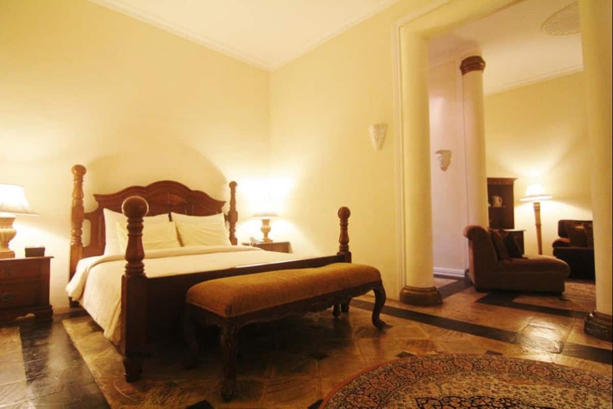 A bedroom with a four-poster bed, a bench, a nightstand, a lamp, and a chair.