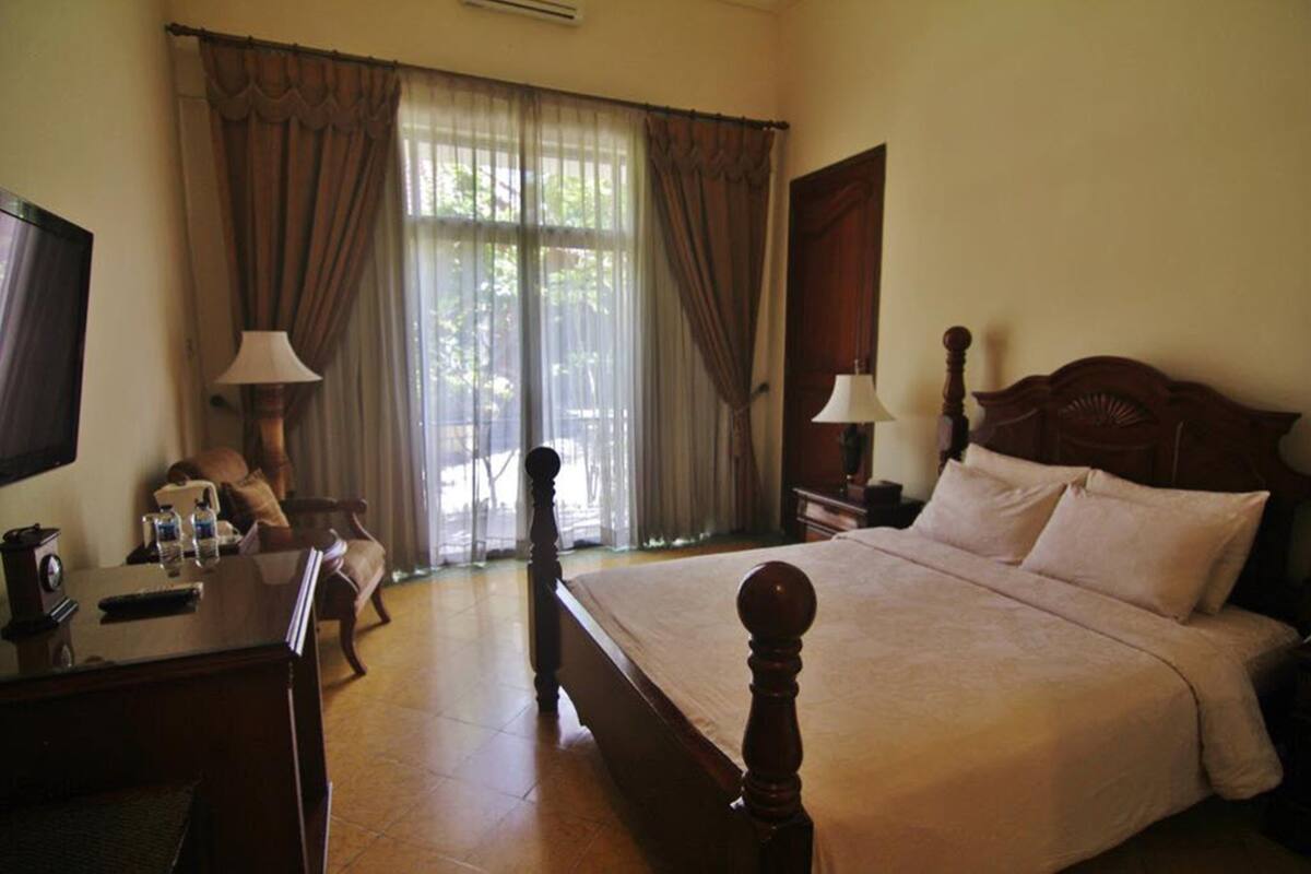 A hotel room with a large bed, two bedside tables with lamps, a desk with a chair, and a TV on the wall.