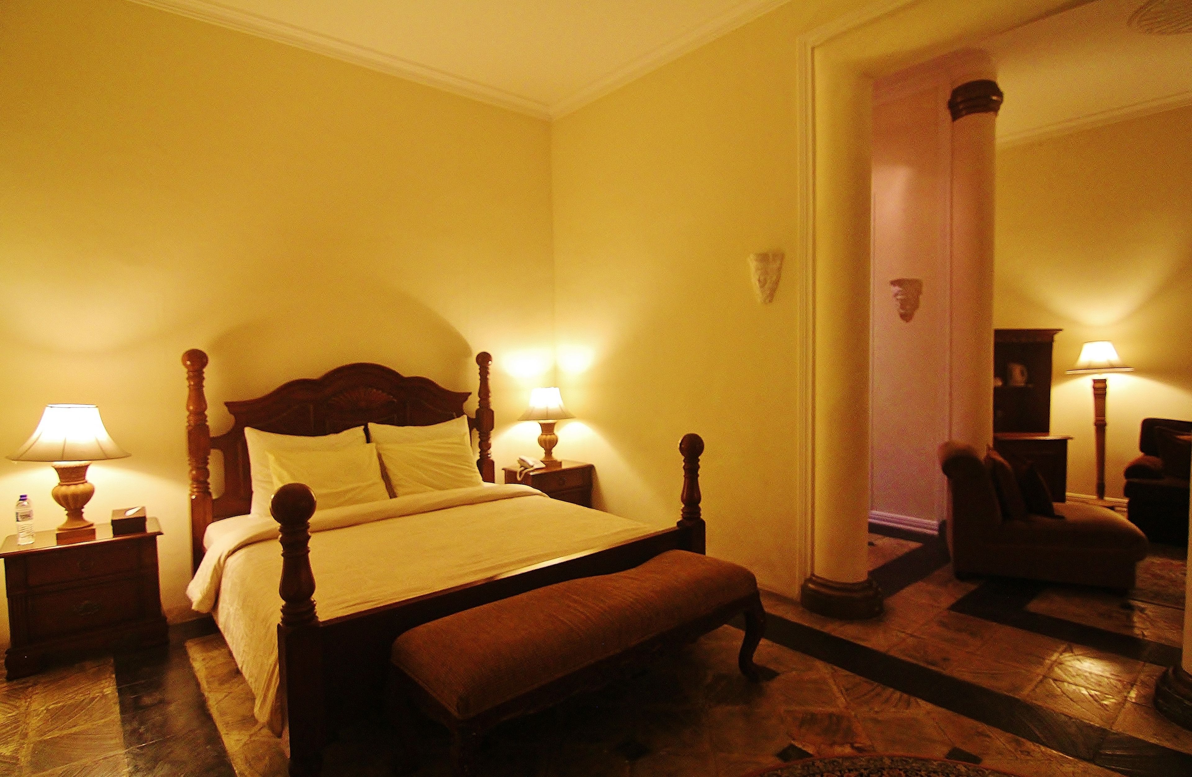 A hotel room with a large bed, two bedside tables with lamps, a bench at the foot of the bed, and a mirror on the wall.