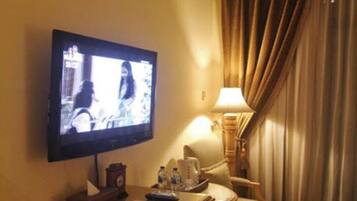 Habitación de hotel con televisión sobre un escritorio de madera, una lámpara, una silla y una ventana con cortinas.