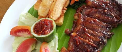A plate of grilled meat, fried plantains, and fresh vegetables on a banana leaf.