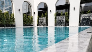 A swimming pool with clear water, surrounded by white walls and arched doorways.