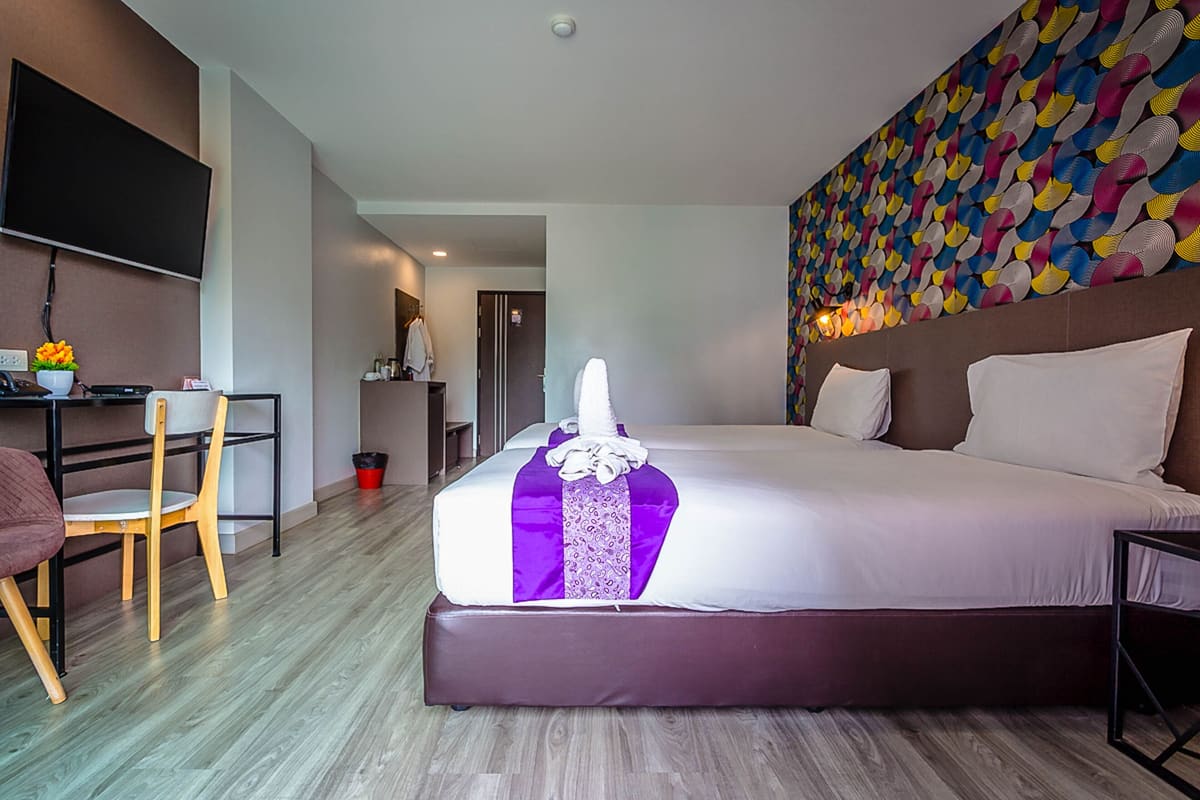A hotel room with a large bed, a desk with a chair, a television, and a colorful wall pattern.