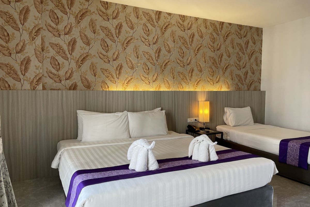 A hotel room with two beds, a large wall with a leaf pattern, a bedside lamp, and towels on the beds.