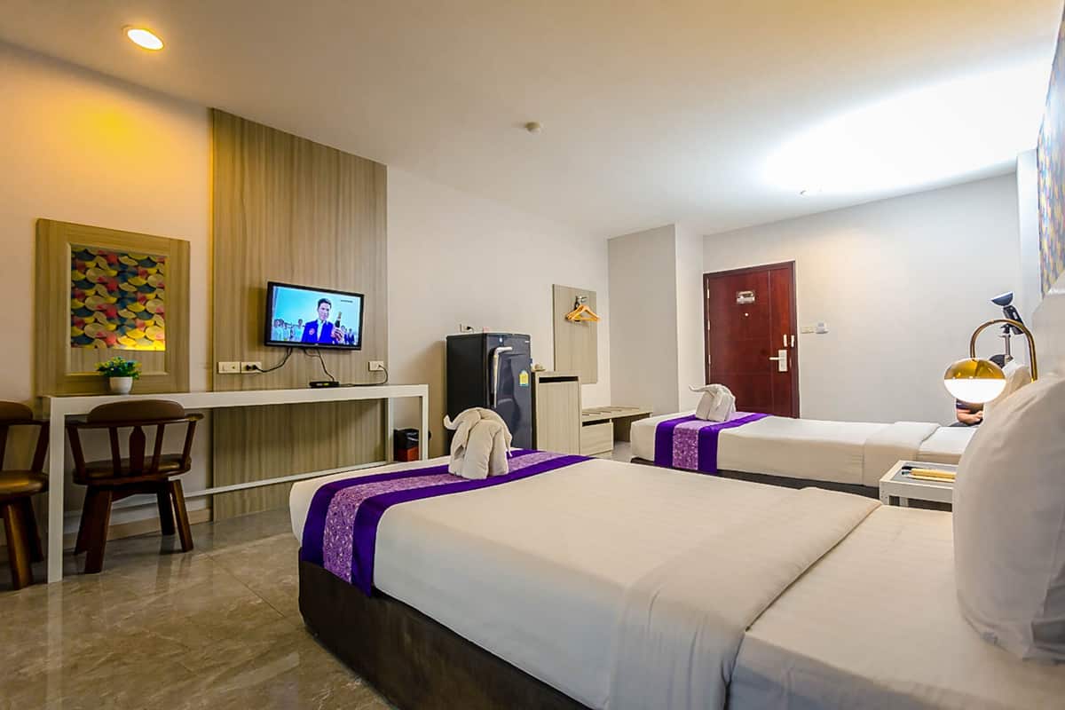 A hotel room with two beds, a desk with a television, a refrigerator, and a door.