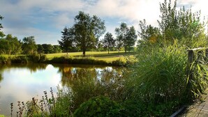 A serene lakeside view with a pathway leading to a grassy area and trees. - Sandford Springs Hotel & Golf Club (Tadley)
