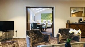 A hotel room with a TV, two armchairs, a coffee table, and a view into the dining area. - Sandford Springs Hotel & Golf Club (Tadley)