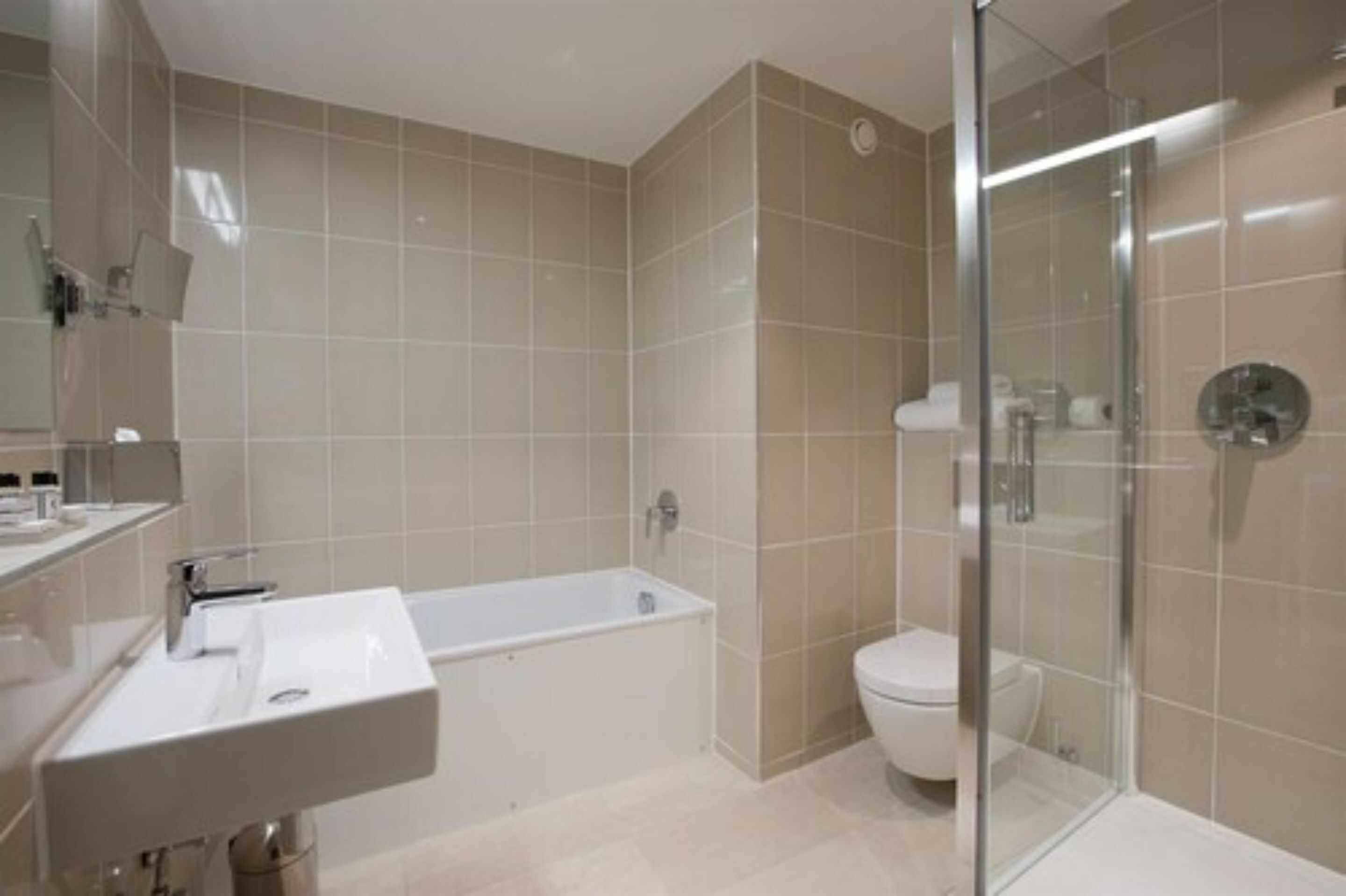 A modern bathroom with a bathtub, toilet, and glass shower enclosure.