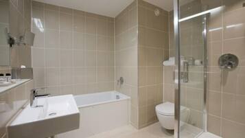 A modern bathroom with a bathtub, toilet, and glass shower enclosure.