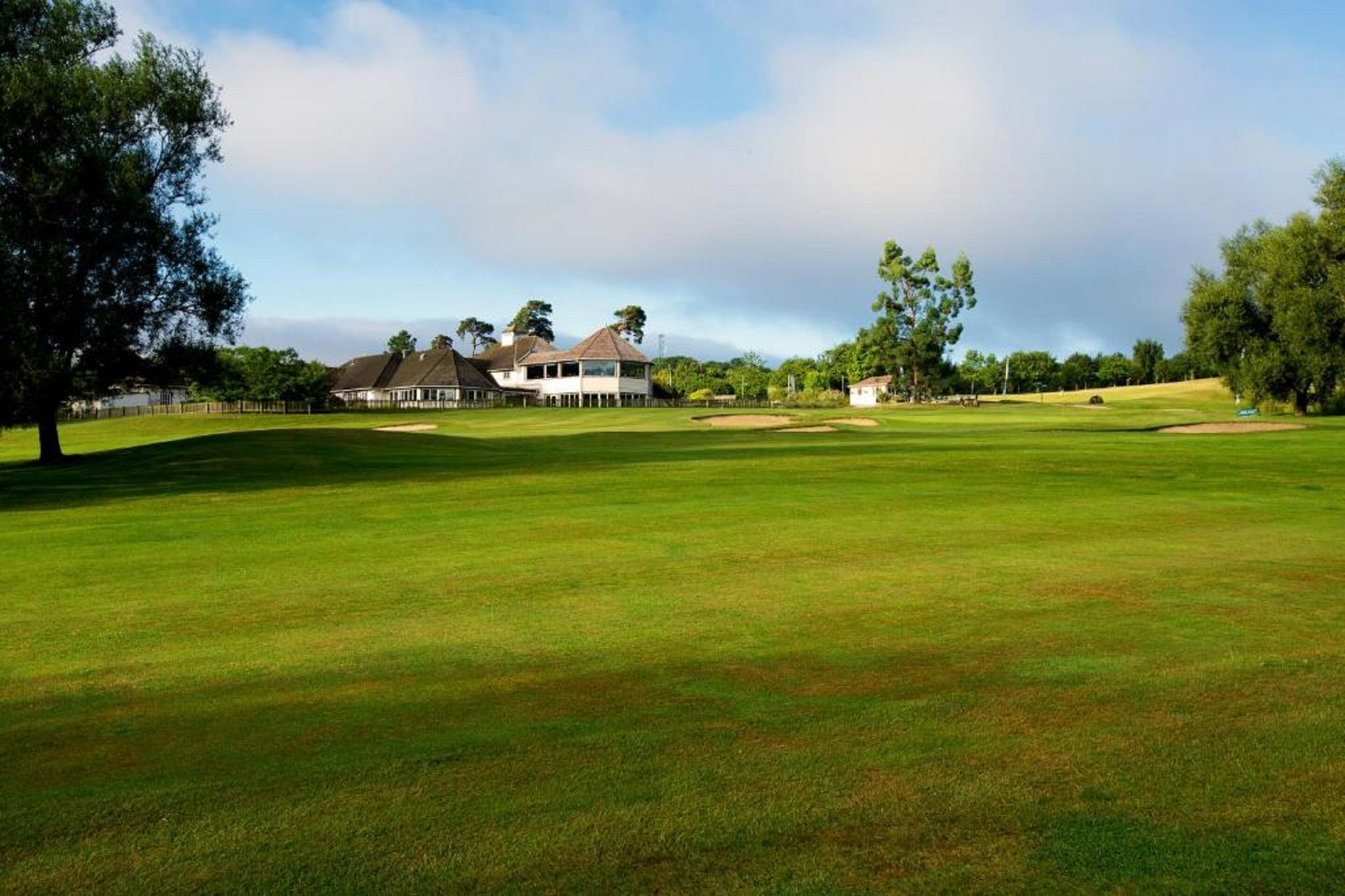 Ein Golfplatz mit Clubhaus, Bäumen und blauem Himmel.