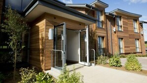 A modern building with a wooden facade, large glass doors, and a covered entrance. - Sandford Springs Hotel & Golf Club (Tadley)