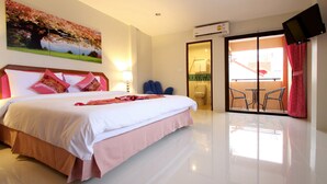A hotel room with a large bed, a balcony with chairs, and a TV mounted on the wall. - Phuket Airport Inn (Sa Khu)