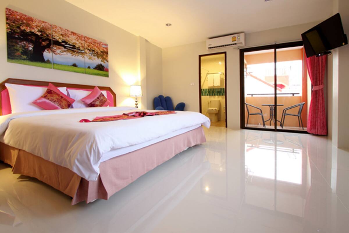 A hotel room with a large bed, a balcony with chairs, and a TV mounted on the wall.